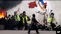 A woman passes by a mural by street artist PBOY depicting Yellow Vest (gilets jaunes) protestors inspired by a painting by Eugene Delacroix, "La Liberte guidant le Peuple" (Liberty Leading the People), in Paris, Thursday, Jan. 10, 2019. 