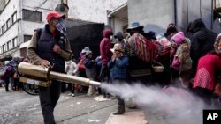 Un trabajador rocía desinfectante alrededor de las personas que viajaron desde las provincias a la iglesia Monte de Oración para comprar alimentos y ropa durante la campaña anual del Buen Samaritano de la iglesia en La Paz, Bolivia, el martes 28 de diciembre de 2021.