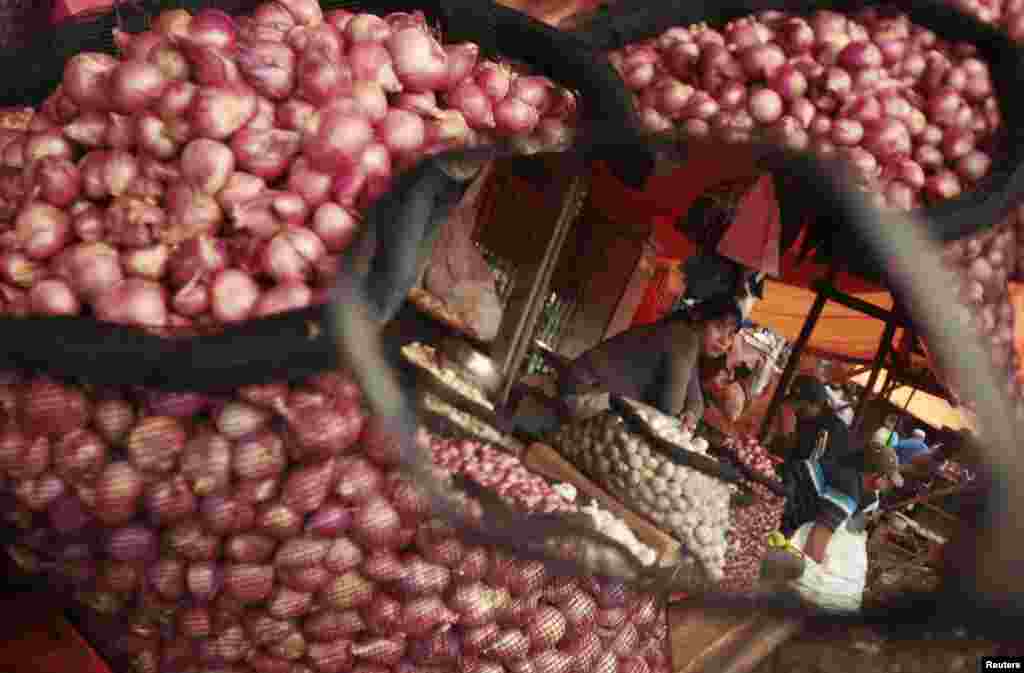 A vendor selling red onions waits for customers at a market in Makassar, Indonesia. Indonesia's Inflation surged to a nearly two-year high in March. The vendor is reflected in a motorcycle's wing mirror.