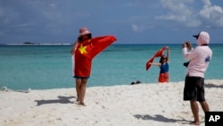 FILE - Chinese tourists take souvenir photos with the Chinese national flag as they visit Quanfu Island, one of Paracel Islands of Sansha prefecture of southern China's Hainan province in the South China Sea, Sept. 14, 2014. 