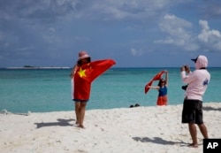 FILE - Chinese tourists take souvenir photos with the Chinese national flag as they visit Quanfu Island, one of Paracel Islands of Sansha prefecture of southern China's Hainan province in the South China Sea, Sept. 14, 2014.