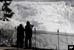 Ice is seen on the side of the Great Falls National Historic Park as a couple takes in the sights during a frigid winter day in Paterson, N.J., Jan. 30, 2019.