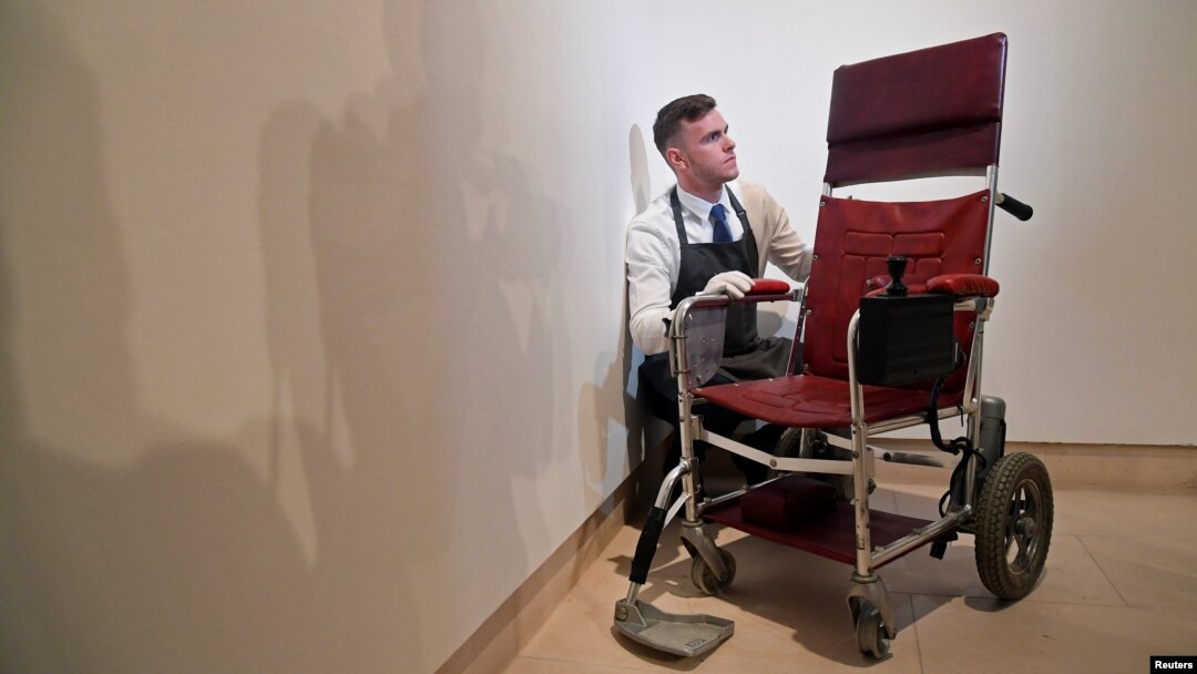 Fine-art handler Tom Richardson poses with a motorized wheelchair belonging to British theoretical physicist Stephen Hawking ahead of an auction of items from Hawkings' personal estate at Christie's in London, Oct. 30, 2018.