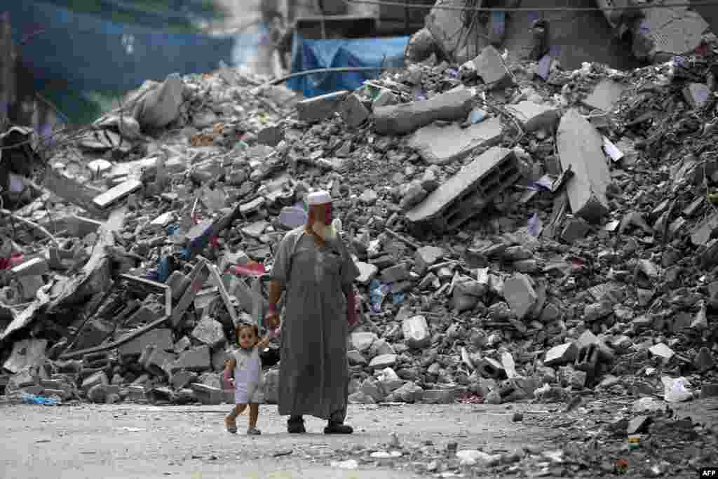 Seorang pria lansia memegang tangan seorang anak saat berjalan melewati sebuah bangunan yang hancur oleh pemboman Israel di kamp pengungsi Bureij di Jalur Gaza tengah pada tanggal 25 Agustus 2024. (AFP)