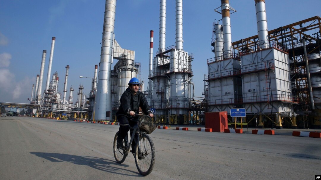 Seorang pegawai perusahaan perminyakan naik sepeda di depan kilang minyak di bagian selatan Teheran, Iran. (Foto: Dok)