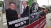 FILE - A photo showing U.S. President Donald Trump and North Korean leader Kim Jong Un is displayed as a member of People's Democratic Party stands to oppose military exercises between the United States and South Korea, near the U.S. Embassy in Seoul, South Korea.