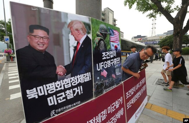 FILE - A photo showing U.S. President Donald Trump and North Korean leader Kim Jong Un is displayed as a member of the People's Democratic Party stands to oppose military exercises between the United States and South Korea near the U.S. embassy in Seoul, South Korea, June 19, 2018.