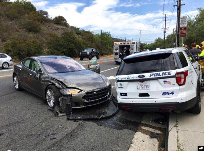 FILE - This photo provided by the Laguna Beach Police Department shows a Tesla sedan, left, in autopilot mode that crashed into a parked police cruiser, in Laguna Beach, Calif., May 29, 2018.