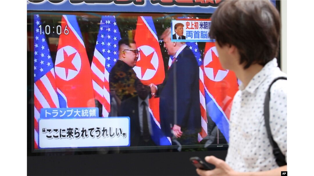 A man looks at a TV screen showing North Korean leader Kim Jong Un, left, and U.S. President Donald Trump shaking hands before their meeting in Singapore, in Tokyo, June 12, 2018. Japanese letters read: "Happy to come here."