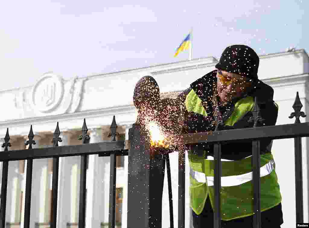 A member of a self-defense unit saws a fence enclosing the parliament building in Kyiv, Feb. 26, 2014.