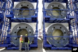 FILE - Workers stand near over-sized racks holding sections of wind turbine towers at a staging site at Port of Providence, in Providence, Rhode Island, July 25, 2016.