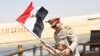 In this picture provided by the office of the Egyptian Presidency, President el-Sissi smiles at a boy dressed in a tiny military uniform as he waves the national flag from a monarchy-era yacht that sailed to the venue of a ceremony for extension of the Su