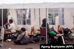Pasien dirawat di bawah tenda yang didirikan di kompleks rumah sakit untuk menangani masuknya orang yang menderita virus corona, di Yogyakarta pada 13 Juli 2021. (Foto: AFP/Agung Supriyanto)