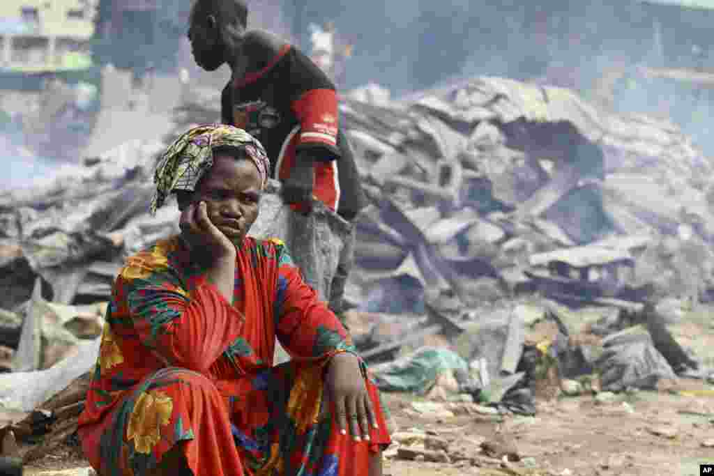 A woman sits near burnt roofing sheets after the Abuja enviromental task force pulled down illegal structures in Utako district in Abuja July 7, 2011. REUTERS/Afolabi Sotunde(NIGERIA - Tags: SOCIETY)