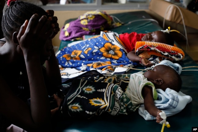 FILE - A mother watches over her child, who is suffering from severe malaria, as other children lay nearby, in the Siaya hospital, Kenya, Oct. 30, 2009.