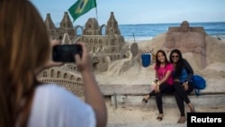 People pose for photos next to a sand sculpture of Pope Francis, Copacabana beach, Rio de Janeiro, July 16, 2013.