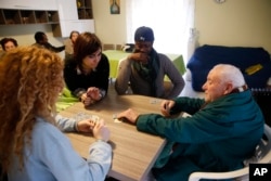 FILE - From left, Italian volunteers Miriam, Federica and migrant form Ghana, Elias Orjini, 24, play cards with Leonardo as they volunteer at an home for the elderly in Catania, Italy, March 25, 2015. (AP Photo/Luca Bruno)