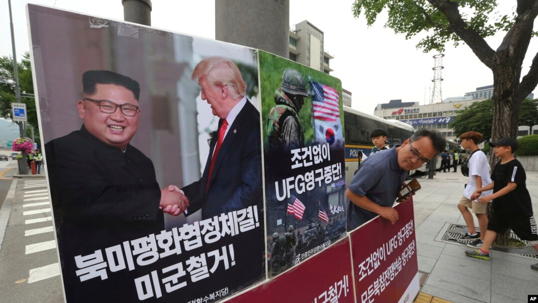 FILE - A photo showing U.S. President Donald Trump and North Korean leader Kim Jong Un is displayed as a member of People's Democratic Party stands to oppose military exercises between the United States and South Korea, near the U.S. Embassy in Seoul, South Korea, June 19, 2018. Trump warned on Aug. 29, 2018, that the United States could at any time restart joint military exercises with South Korea and Japan if progress stalled on North Korean denuclearization.