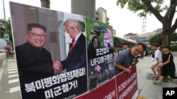 FILE - A photo showing U.S. President Donald Trump and North Korean leader Kim Jong Un is displayed as a member of People's Democratic Party stands to oppose military exercises between the United States and South Korea, near the U.S. Embassy in Seoul, South Korea, June 19, 2018. Trump warned on Aug. 29, 2018, that the United States could at any time restart joint military exercises with South Korea and Japan if progress stalled on North Korean denuclearization.