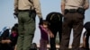Una niña observa cómo los migrantes de Guatemala se quitan los cordones de los zapatos cuando son procesados inicialmente después de entregarse a las autoridades en la frontera entre Estados Unidos y México el 12 de mayo de 2021 en Yuma, Arizona.