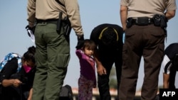 Una niña observa cómo los migrantes de Guatemala se quitan los cordones de los zapatos cuando son procesados inicialmente después de entregarse a las autoridades en la frontera entre Estados Unidos y México el 12 de mayo de 2021 en Yuma, Arizona.