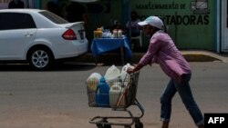 Una mujer empuja un carrito cargado con botellas de agua recolectadas de un grifo improvisado en una calle de Maracaibo, Venezuela, el 25 de mayo de 2020, durante la pandemia del coronavirus COVID-19.
