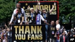 Gelandang AS Megan Rapinoe (tengah) memegang trofi Piala Dunia, gelandang Carli Lloyd (kiri), Walikota New York City Bill de Blasio (kiri belakang), dan kepala pelatih Jill Ellis (kanan) melambai ke arah penonton pada parade untuk merayakan kemenangan tim nasional putri AS dalam kejuaraan Piala Dunia 2015.