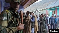 A member of the Indian Border Security Force stands guard as people wait to vote at a polling station during the third and final phase of the assembly election, in north Kashmir's Bandipora district, Oct.1, 2024.