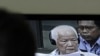 A journalist listens to Khieu Samphan, center, former Khmer Rouge head of state, as he appears on TV screen at the court press center of the U.N.-backed war crimes tribunal in Phnom Penh, file photo. 