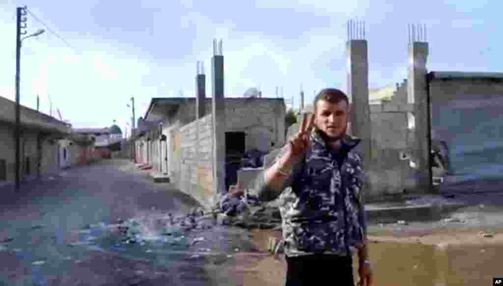 A Free Syrian Army soldier flashes the victory sign as damages caused by warplanes and rocket launchers is seen at background in Hama, Syria, January 28, 2013. Image taken from video.