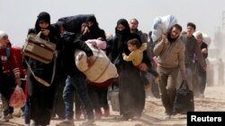 FILE - People walk with their belongings as they flee the rebel-held town of Hammouriyeh, eastern Ghouta, Syria, March 15, 2018. 