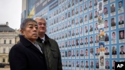 Japan's Foreign Minister Takeshi Iwaya, left, and Ukraine's Foreign Minister Andriiy Sybiha look at photos of fallen soldiers after a flower laying ceremony at the memorial wall in Kyiv, Ukraine, Nov. 16, 2024.