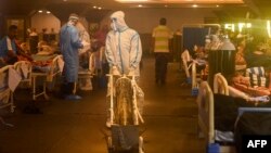 Health workers wearing personal protective equipment (PPE kit) attends to Covid-19 coronavirus positive patients inside a banquet hall temporarily converted into a covid care centre in New Delhi on April 28, 2021. (Photo by Prakash SINGH / AFP)