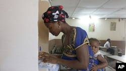 A woman with a baby on her back, votes at a polling station in Abidjan, Ivory Coast, December 11, 2011.