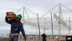 FILE - A worker carries a equipment as he walks past the aquatic stadium under construction at the Olympic Park of the 2016 Olympics in Rio de Janeiro, Brazil, March 23, 2015. 