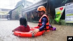 Seorang petgas penyelamat membantu seorang anak perempuan saat mereka berusaha menerja banjir yang disebabkan olah Topan Rai di Cagayan de Oro City, selatan Filipina, pada 16 Desember 2021. (Foto: Philippine Coast Guard via AP)