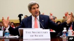 El secretario de Estado, John Kerry habla en la Cámara de Representantes, mientras en el fondo se elevan manos rojas de manifestantes opuestos a un ataque militar en Siria.