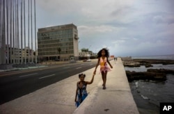 A girls holds her mother's hand, as she walks on the Malecon sea wall, past the the US embassy in Havana, Cuba, Aug. 11, 2015.