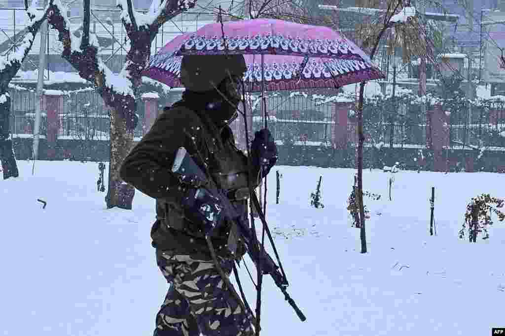 An Indian paramilitary trooper carries an umbrella as he walks through a park during snowfall in Srinagar.