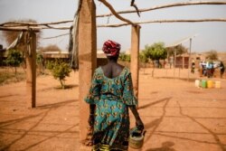 FILE - A displaced woman walks with a kettle in the Kaya camp, 100 kms North of Ouagadougou, Burkina Faso, Feb. 8, 2021.