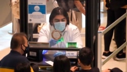 A TSA agent checks IDs of air travelers wearing masks and separated by plexiglass at Love Field in Dallas, Dec. 31, 2021.