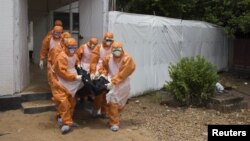FILE - Members of a burial team, wearing protective suits, remove a body from an Ebola holding center at the Port Loko District Hospital in Sierra Leone Sept. 27, 2014. 
