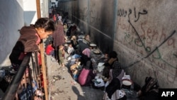 Anak-anak menyaksikan para perempuan duduk membuat roti pipih tradisional di sepanjang gang di Rafah di Jalur Gaza selatan pada 1 November 2023 di tengah pertempuran yang sedang berlangsung antara Israel dan Hamas Palestina. (Foto: AFP)