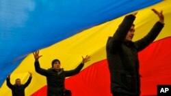 FILE - People walk under a huge Moldovan national flag, in Chisinau, Moldova, Nov. 14, 2016.