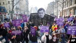 ARCHIVO - Mujeres marchan para conmemorar el Día Internacional de la Mujer, una de ellas con un cartel que muestra al ministro del Interior francés, Gerald Darmanin, quien fue acusado por una mujer de violarla en 2009, el lunes 8 de marzo de 2021 en París. 