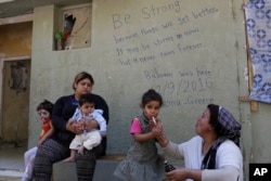 In this photo taken on Sept. 13, 2016, a Kurd Syrian mother gives cough syrup to her child at Ritsona refugee camp north of Athens.