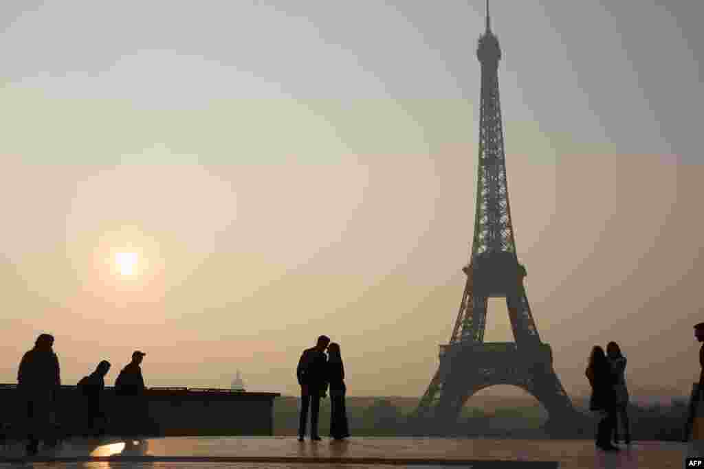 Mọi người qua lại phía trước tháp Eiffel lúc mặt trời mọc ở Paris, Pháp.