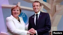 German Chancellor Angela Merkel and French President Emmanuel Macron hold hands after leaving books at the peace library at the Paris Peace Forum as part of the commemoration ceremony for Armistice Day, 100 years after the end of World War I, in Paris, Nov. 11, 2018.