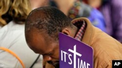 Mpagi Kirumira Michael, from Uganda, holds a sign as he bows his head during a media event where supporters of LBGT rights spoke out against the Methodist Church in Portland.