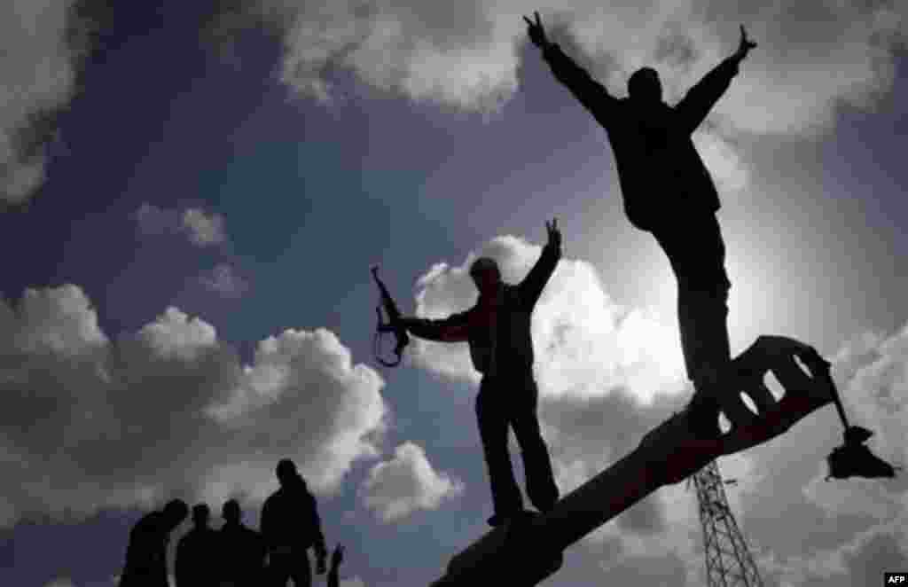 Libyan people celebrate on a tank belonging to the forces of Moammar Gadhafi in the outskirts of Benghazi, eastern Libya, Sunday, March 20, 2011. The tanks were destroyed earlier by NATO planes. The U.S. military said 112 Tomahawk cruise missiles were fir